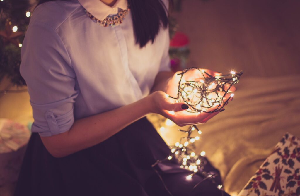 A woman gently cradles a glowing string of Christmas lights in a cozy indoor setting.